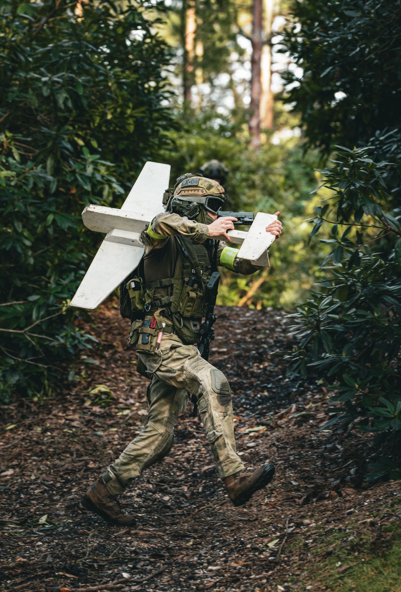 A soldier carrying a fixed-wing unmanned aircraft through wooded terrain.